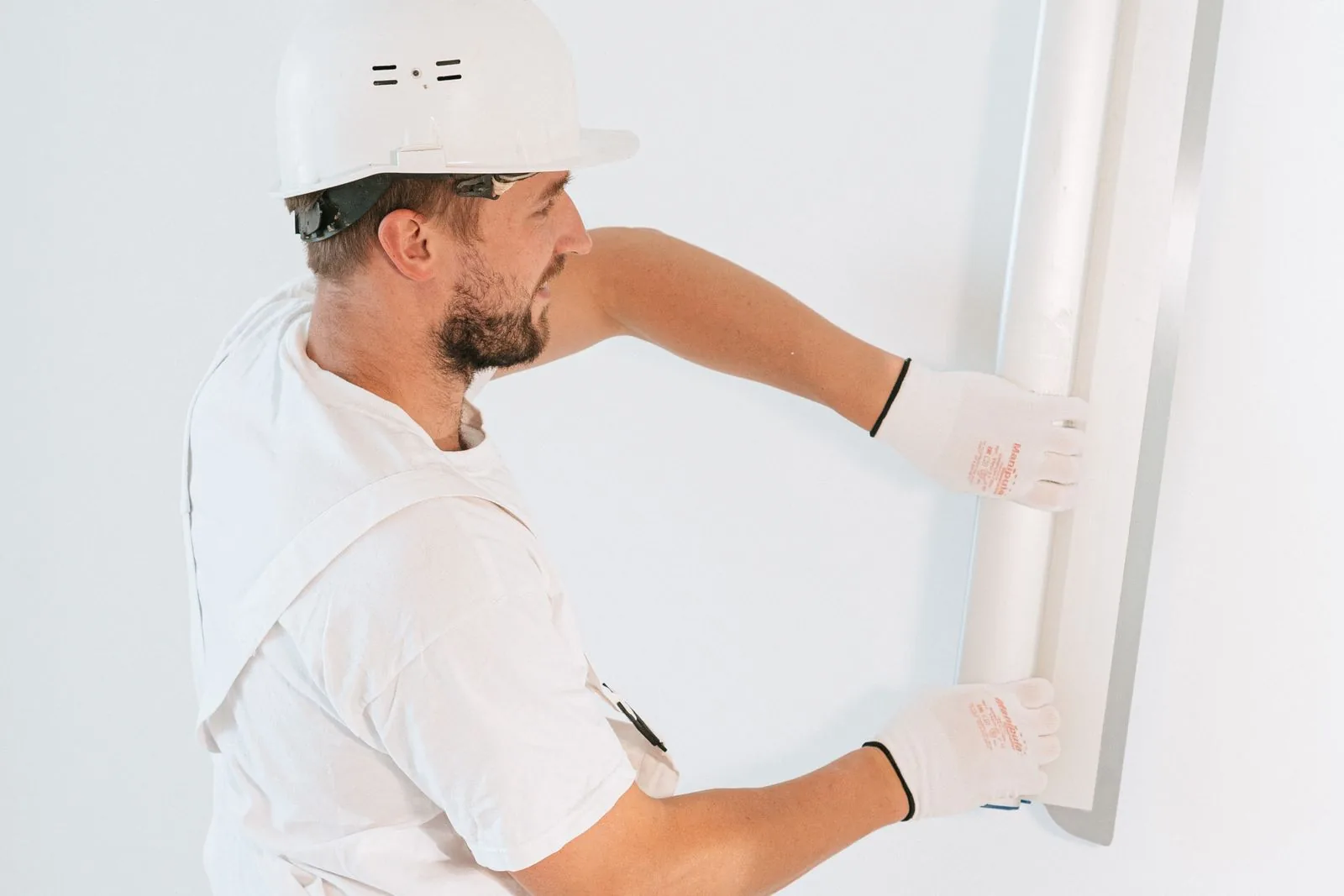 Construction worker installing drywall wearing gloves and helmet